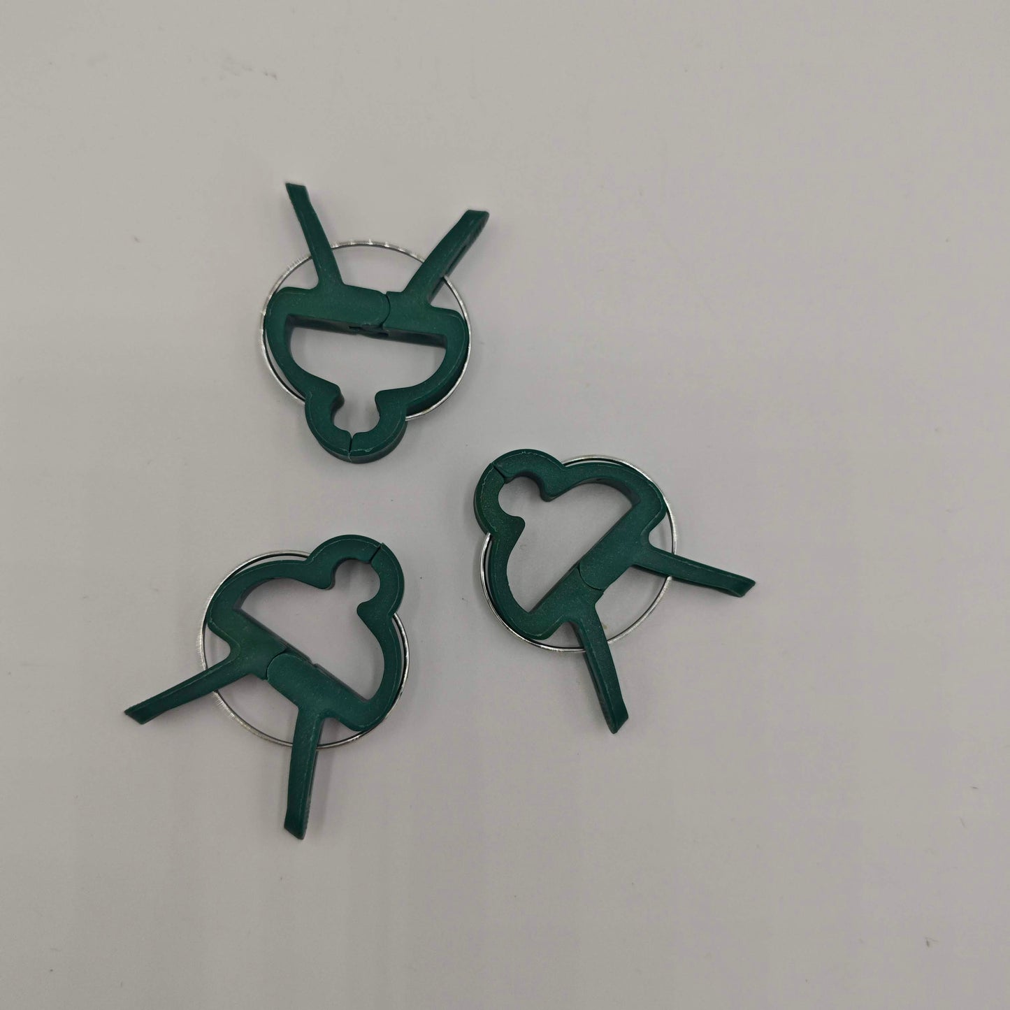 Un lot de trois clips de support pour plantes en plastique vert avec un ressort métallique, conçus pour fixer les tiges aux tuteurs.