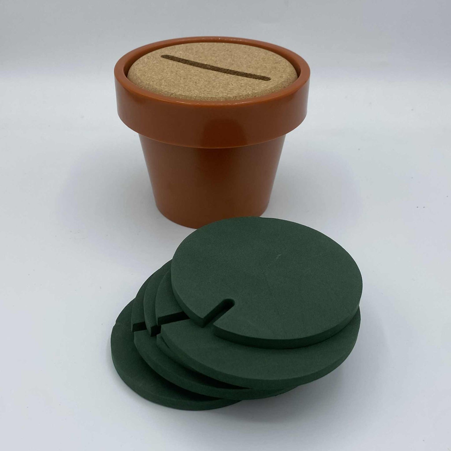 Un ensemble de dessous de verre créatifs en forme de feuilles vert foncé, rangés dans un support qui ressemble à un pot de fleur en terre cuite avec un couvercle en liège.