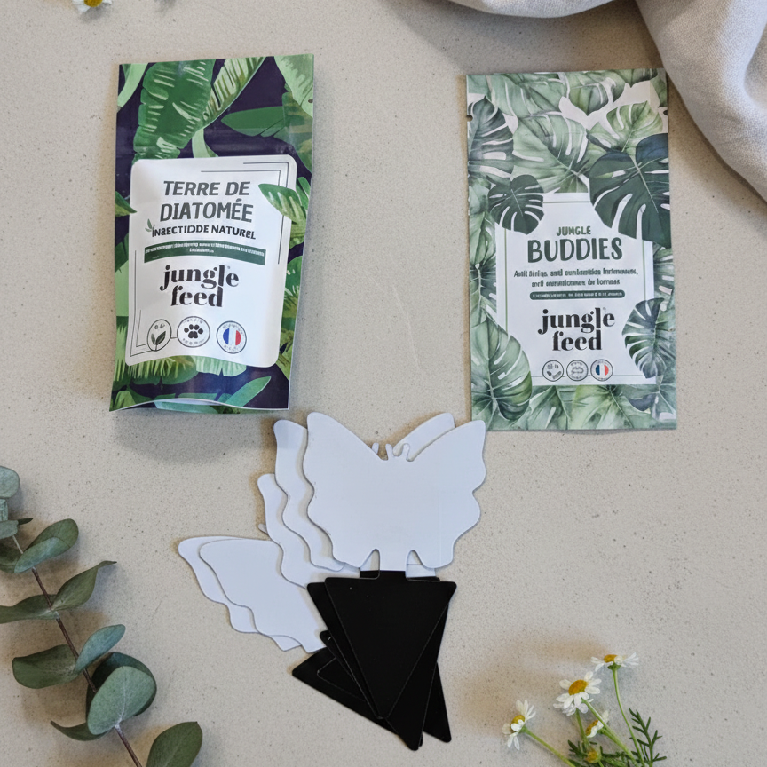 Une vue de dessus présentant le contenu du pack Jungle Feed : un sachet de Terre de Diatomée, un sachet de nématodes Jungle Buddies, et plusieurs pièges collants blancs en forme de papillons posés sur une surface beige à côté de fleurs de camomille.