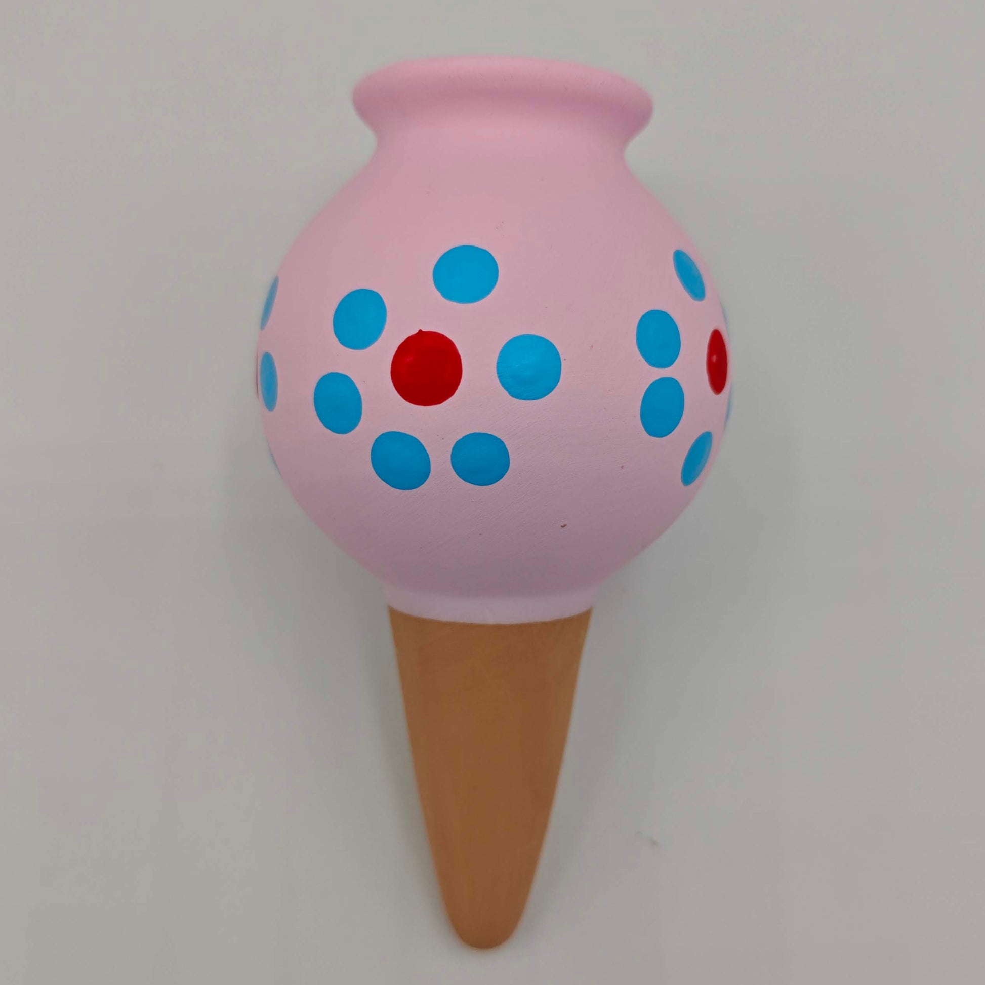 Un cône d'arrosage goutte à goutte pour plantes d'intérieur, en céramique peinte en rose avec des points rouges et bleus.