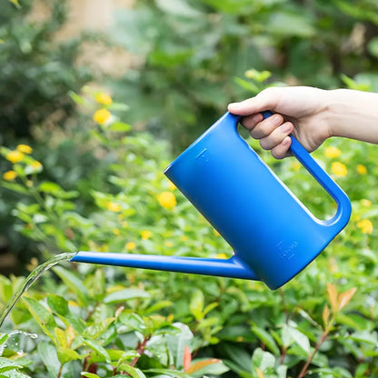 Une main tenant un arrosoir bleu minimaliste, arrosant des plantes en extérieur