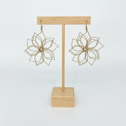 Paire de boucles d'oreilles artisanales en forme de fleur présentées sur un support en bois clair, fond blanc épuré.