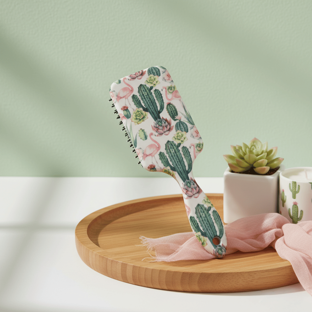 Brosse à cheveux démêlante avec un motif de cactus et de flamants roses, posée sur un plateau en bois avec une plante grasse et une bougie en arrière-plan.
