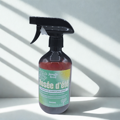  Un flacon pulvérisateur brun de la marque "jungle feed" contenant un produit appelé "Rosée d'été", posé sur une surface blanche avec un fond gris clair et des ombres.