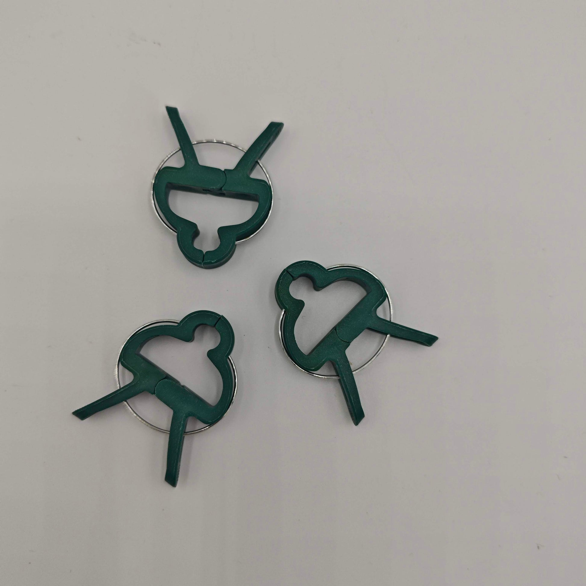 Un lot de trois clips de support pour plantes en plastique vert avec un ressort métallique, conçus pour fixer les tiges aux tuteurs.