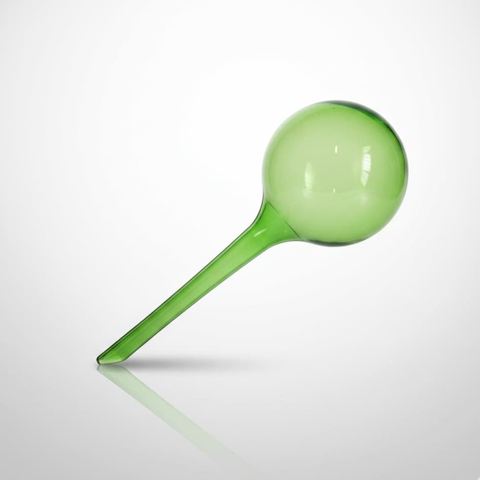 Globe d'arrosage automatique en verre vert translucide sur un fond dégradé gris et blanc avec un reflet élégant.