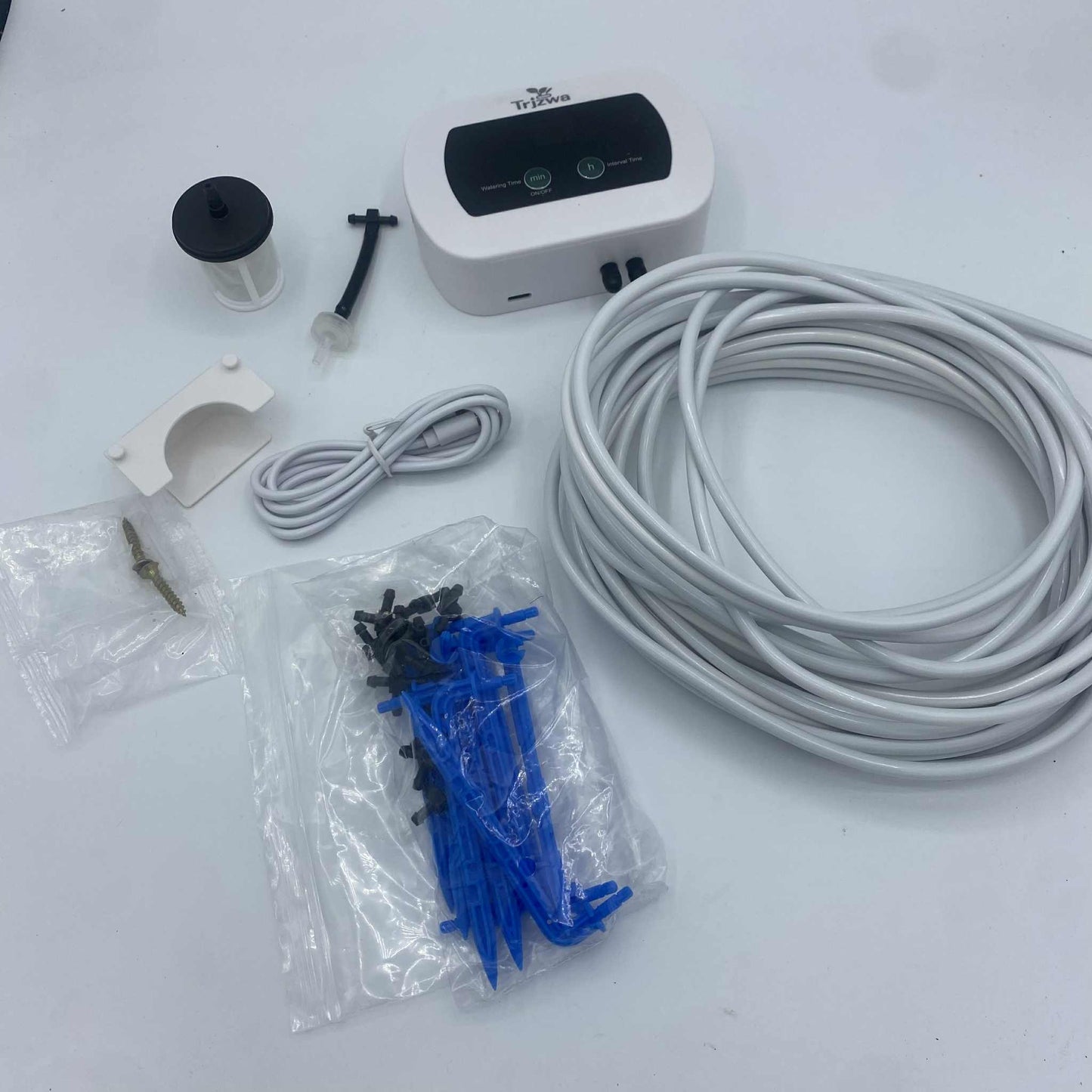 Le contenu d'un kit d'arrosage automatique, avec le programmateur, le tuyau, les piquets de goutte-à-goutte et divers accessoires, posé sur un fond blanc.