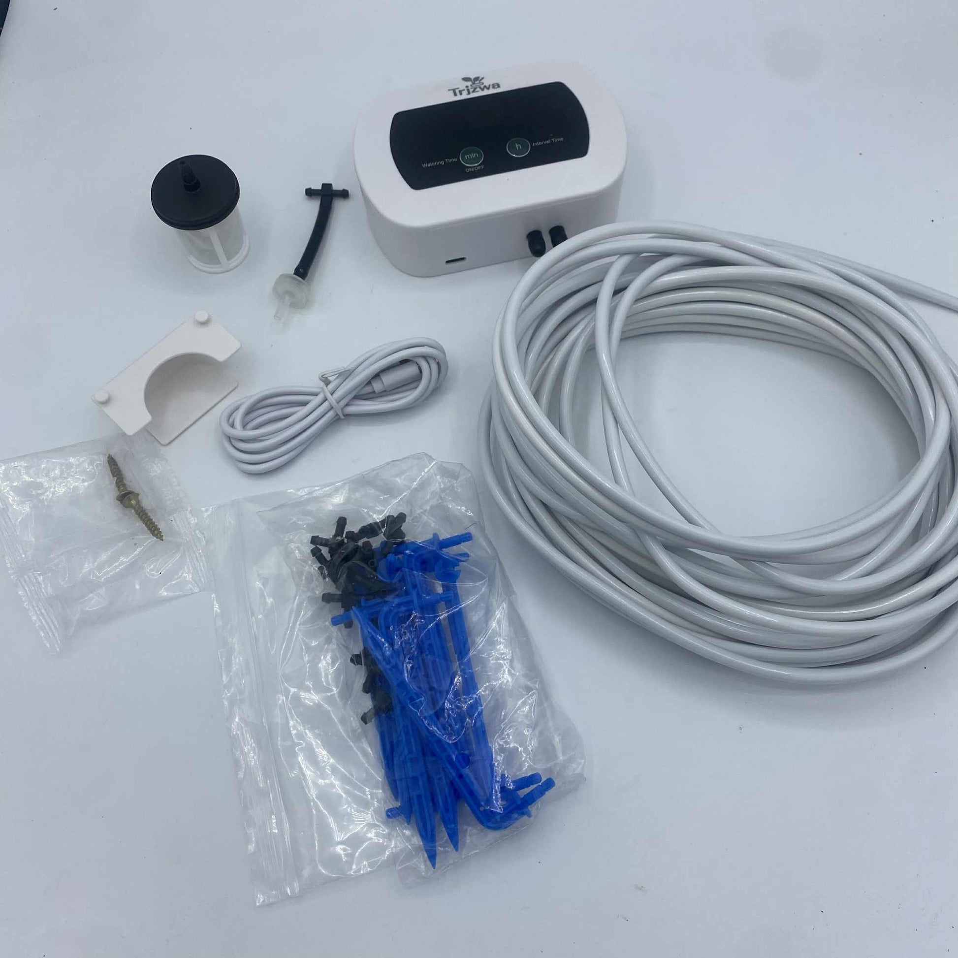 Le contenu d'un kit d'arrosage automatique, avec le programmateur, le tuyau, les piquets de goutte-à-goutte et divers accessoires, posé sur un fond blanc.