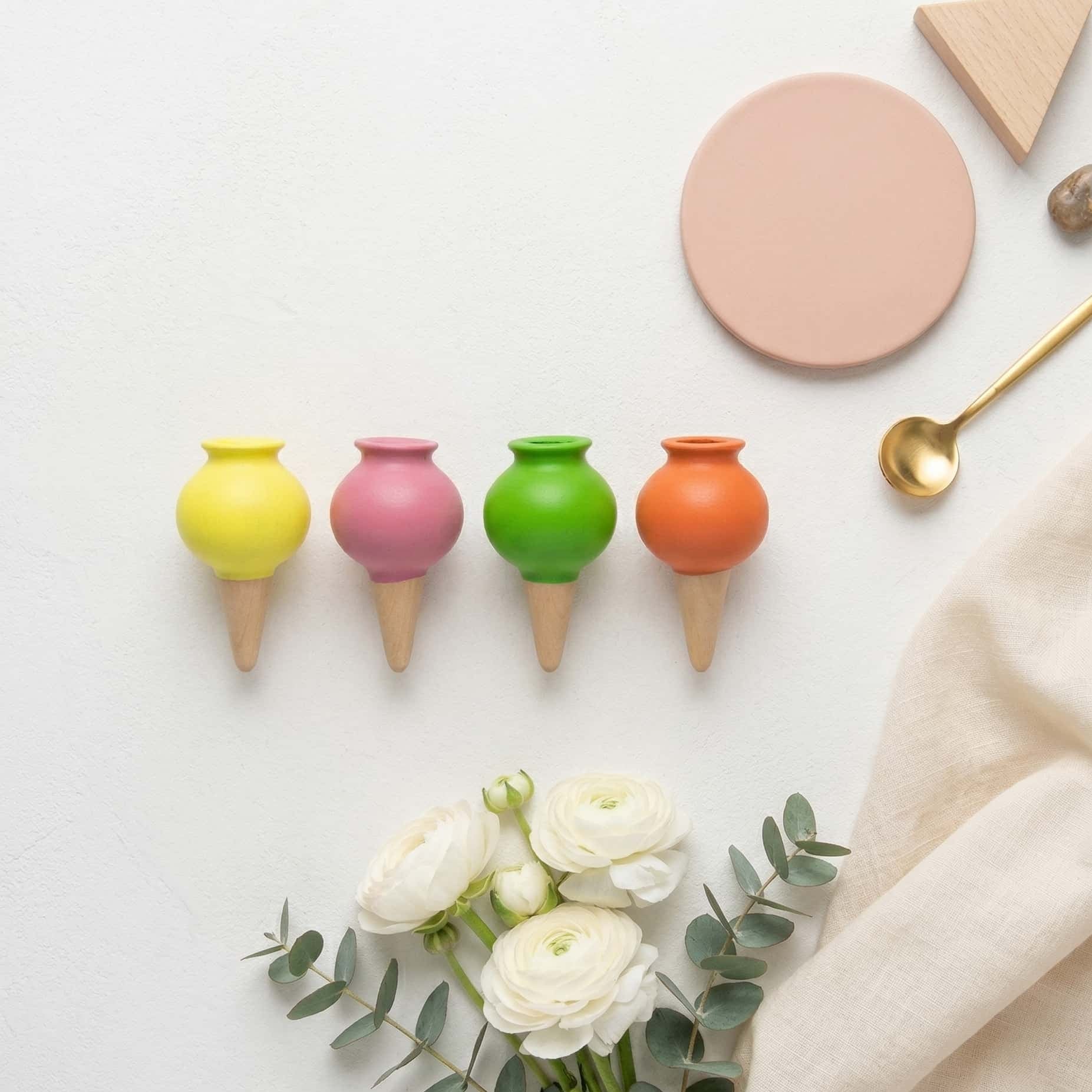 Vue de dessus d'un pack de 4 ollas colorées disposées à plat à côté de fleurs blanches, d'une cuillère dorée et d'accessoires de décoration dans une ambiance douce et lumineuse.