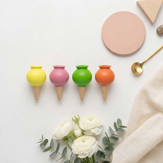 Vue de dessus d'un pack de 4 ollas colorées disposées à plat à côté de fleurs blanches, d'une cuillère dorée et d'accessoires de décoration dans une ambiance douce et lumineuse.