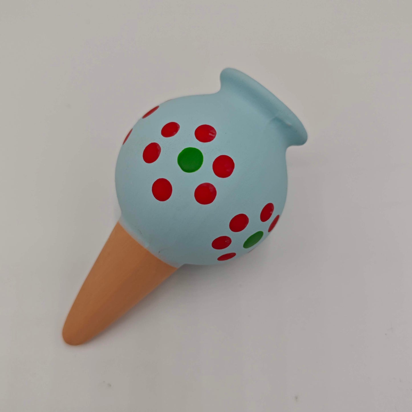 Un cône d'arrosage goutte à goutte pour plantes d'intérieur, en céramique peinte en bleu avec des points rouges et verts.
